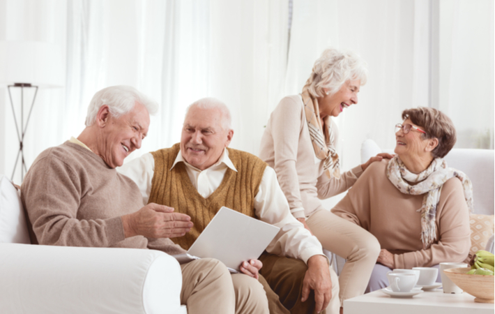 Senior friends laughing and socializing on couch in senior community