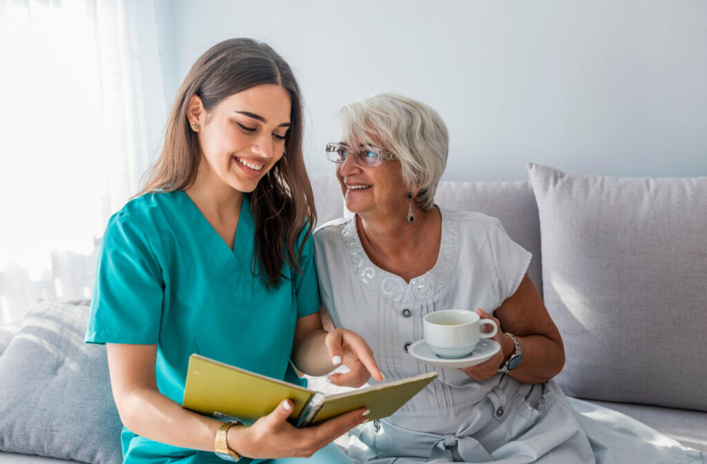 A caregiver flipping through a photo album after bringing a smiling resident their afternoon tea in assisted living.